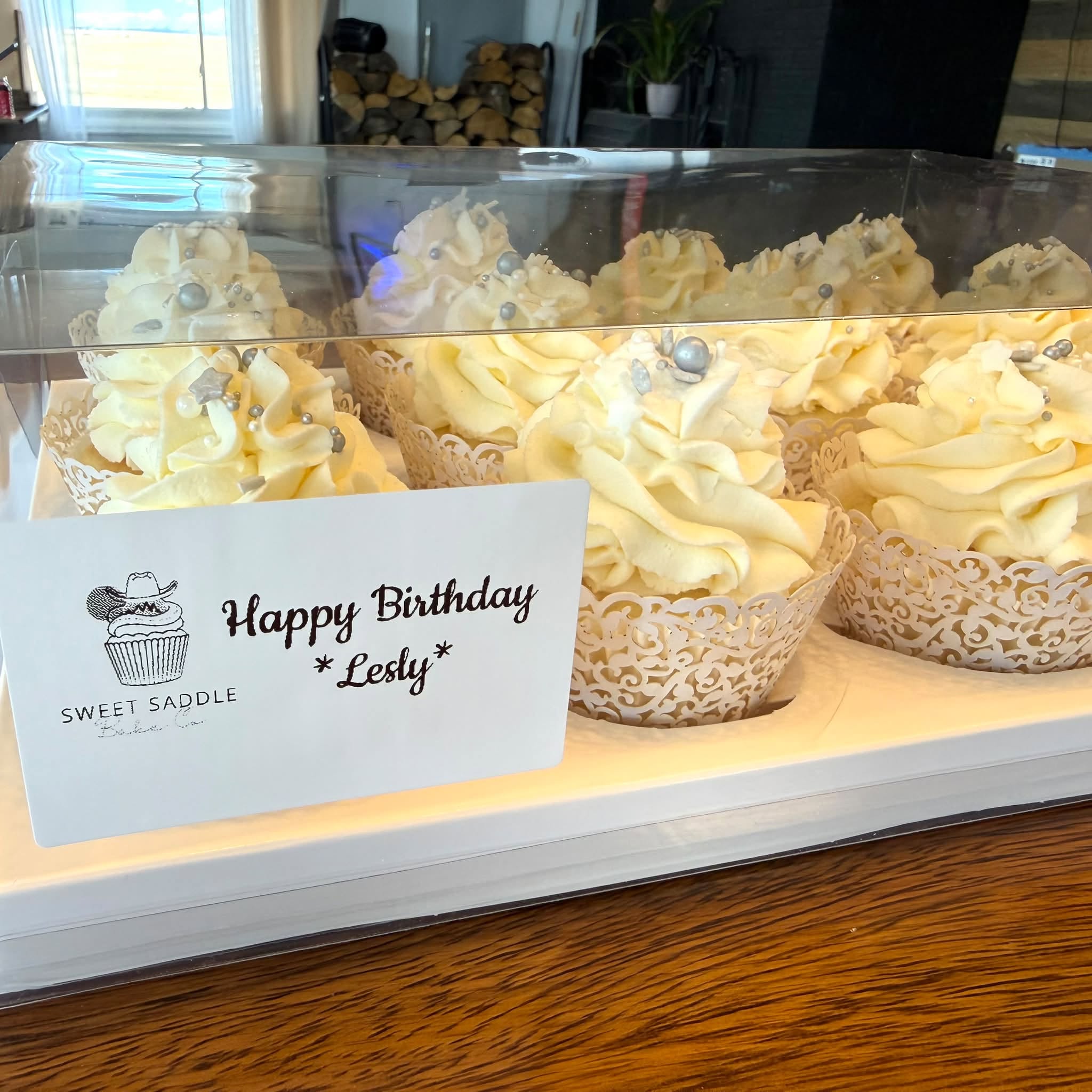 A box of vanilla cupcakes with silver pearls in lace wrappers and a Sweet Saddle happy birthday card