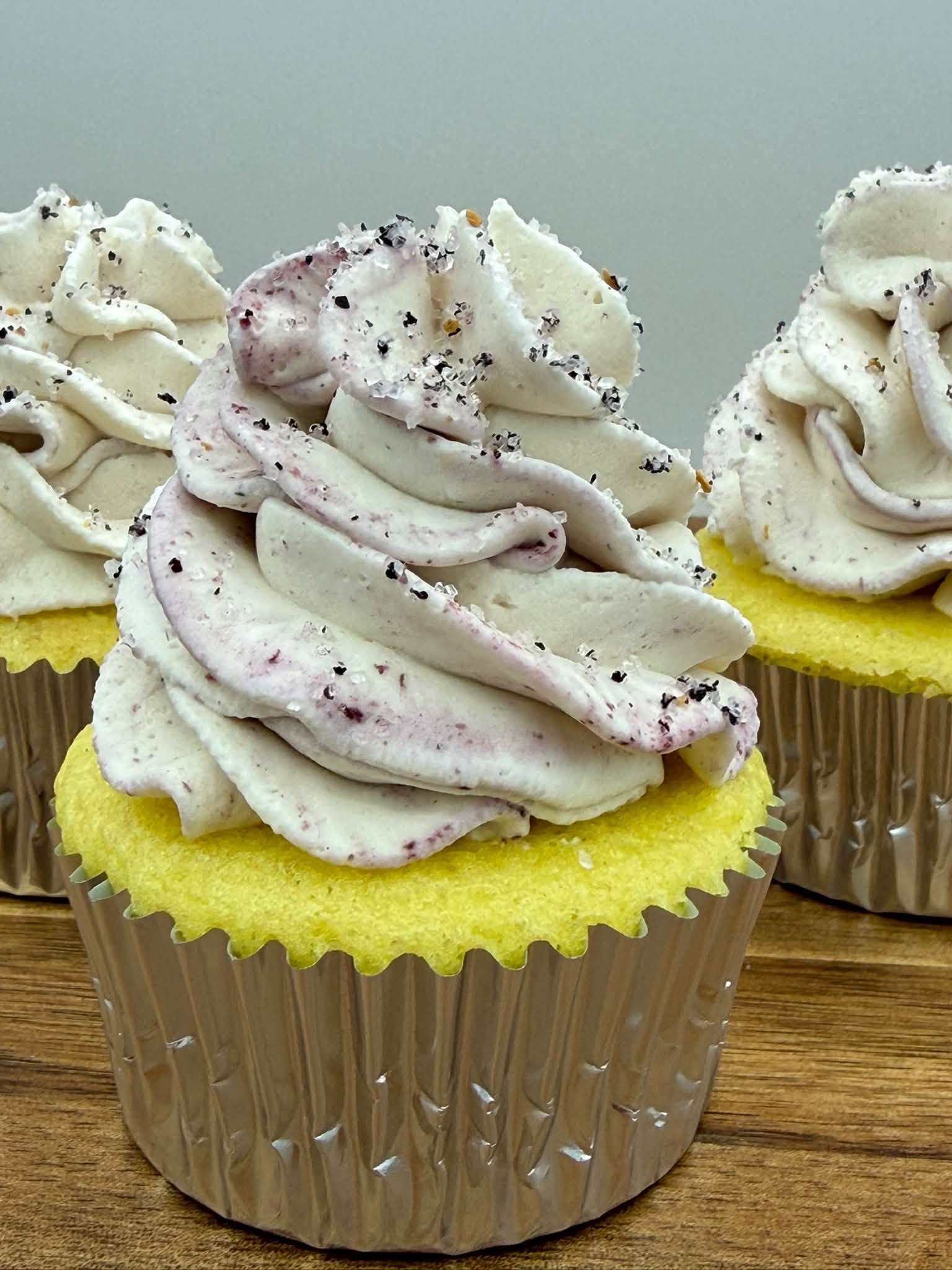 Golden cupcake topped with a tall swirl of berry-streaked buttercream and coarse sugar