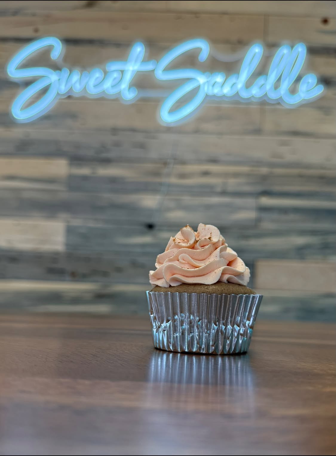 Spiced cupcake with peach buttercream and a dusting of spice beneath the neon sign