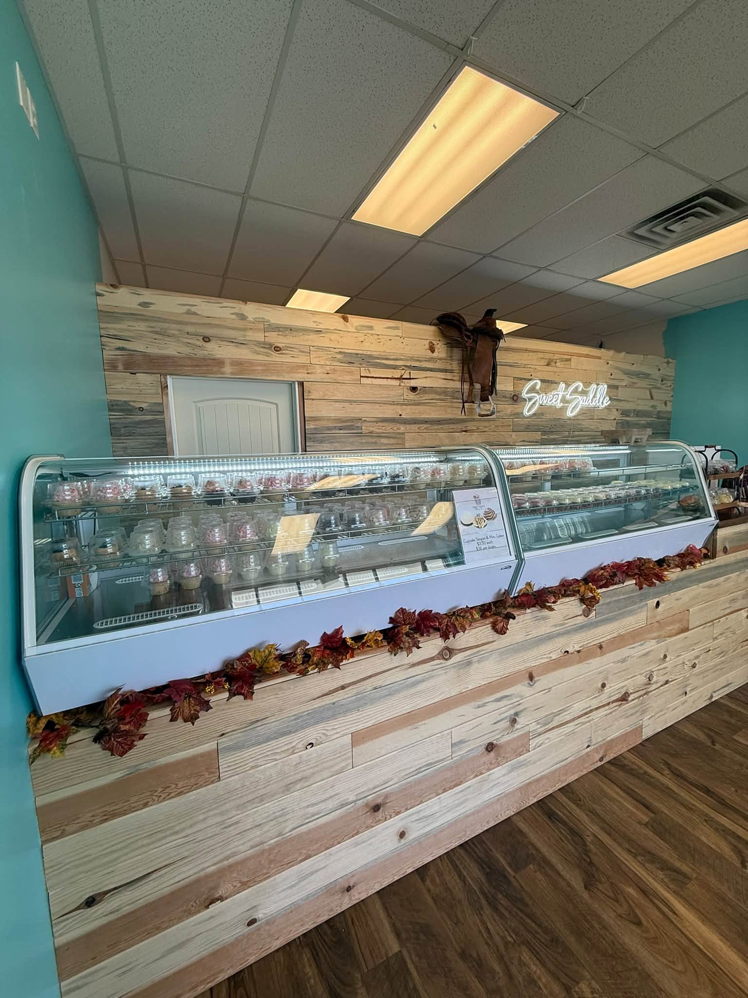 Inside the shop: turquoise walls, a pine counter, a saddle above and a long cupcake case